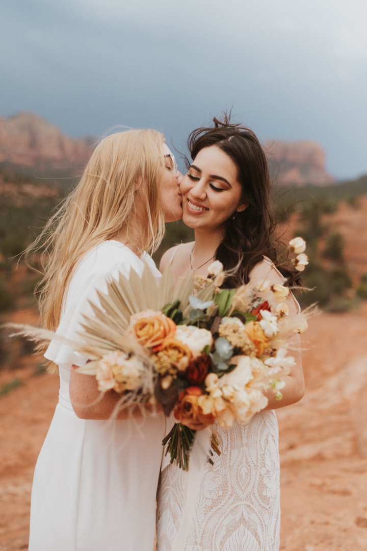 Two brides embracing with a floral bouqet