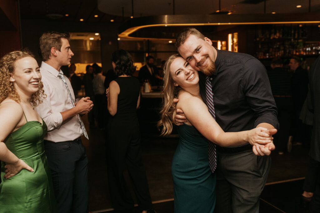 A man and a woman dance together and smile for a photo at a wedding reception. 