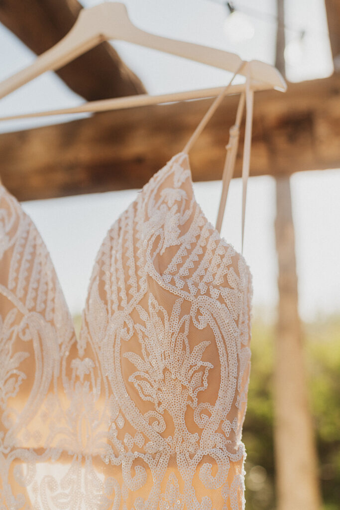 A close up photo of a wedding dress with lace and beading on a hanger.