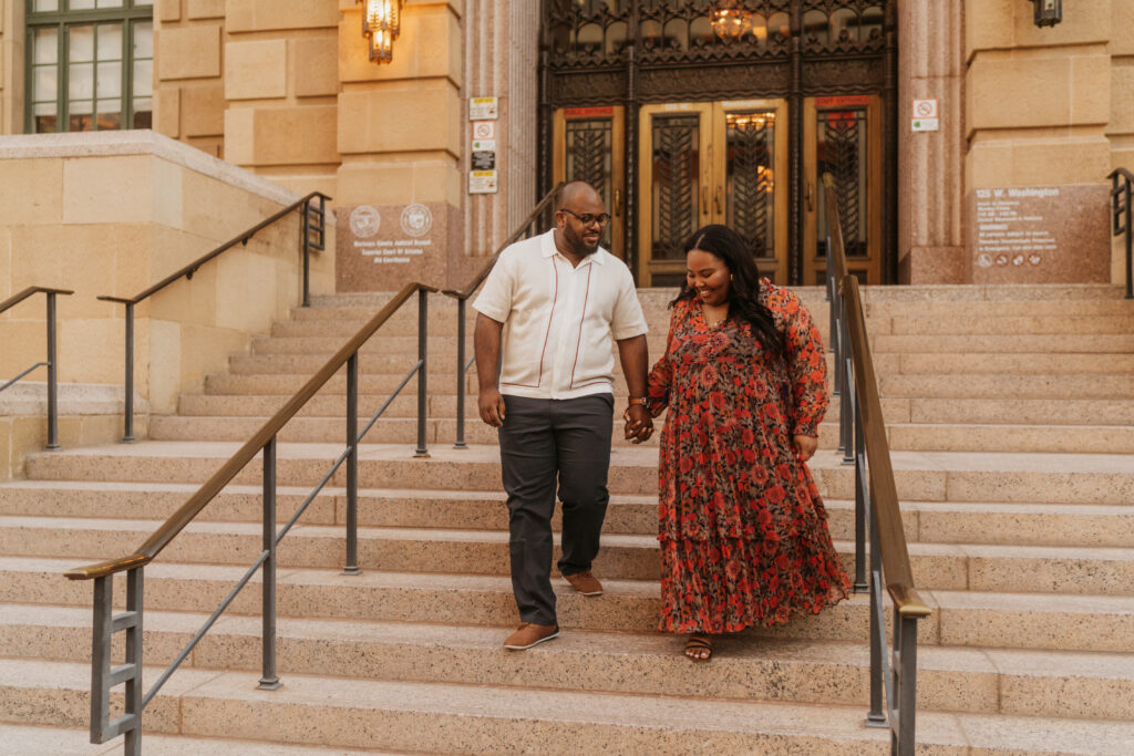 A man and a woman walk down the steps of phoenix city hall holding hands