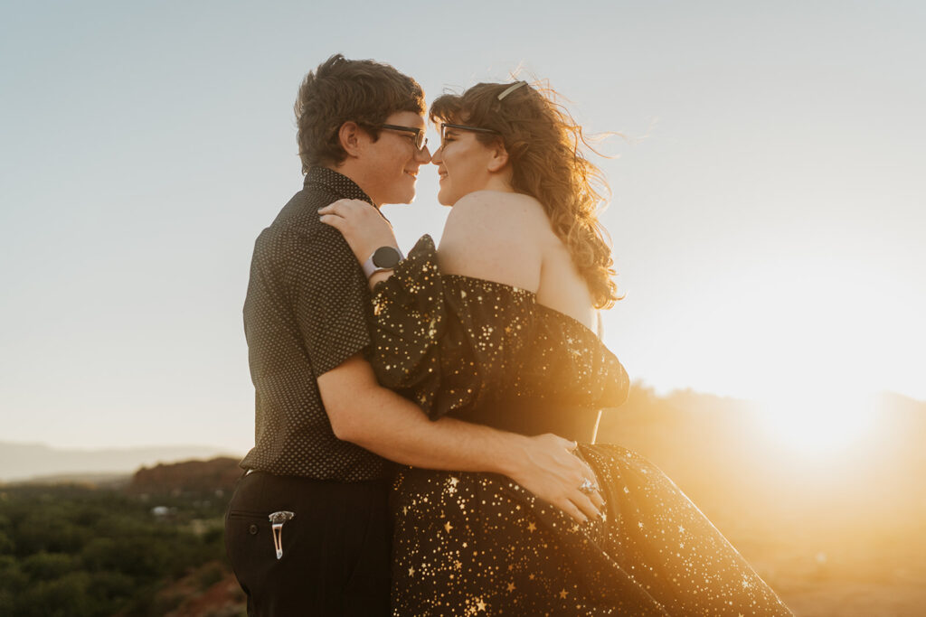 Man and a woman embrace facing one another with the sunset behind them
