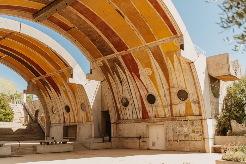 Tall arched buildings painted read and yellow form a outdoor ampetheather at Arcosanti. 