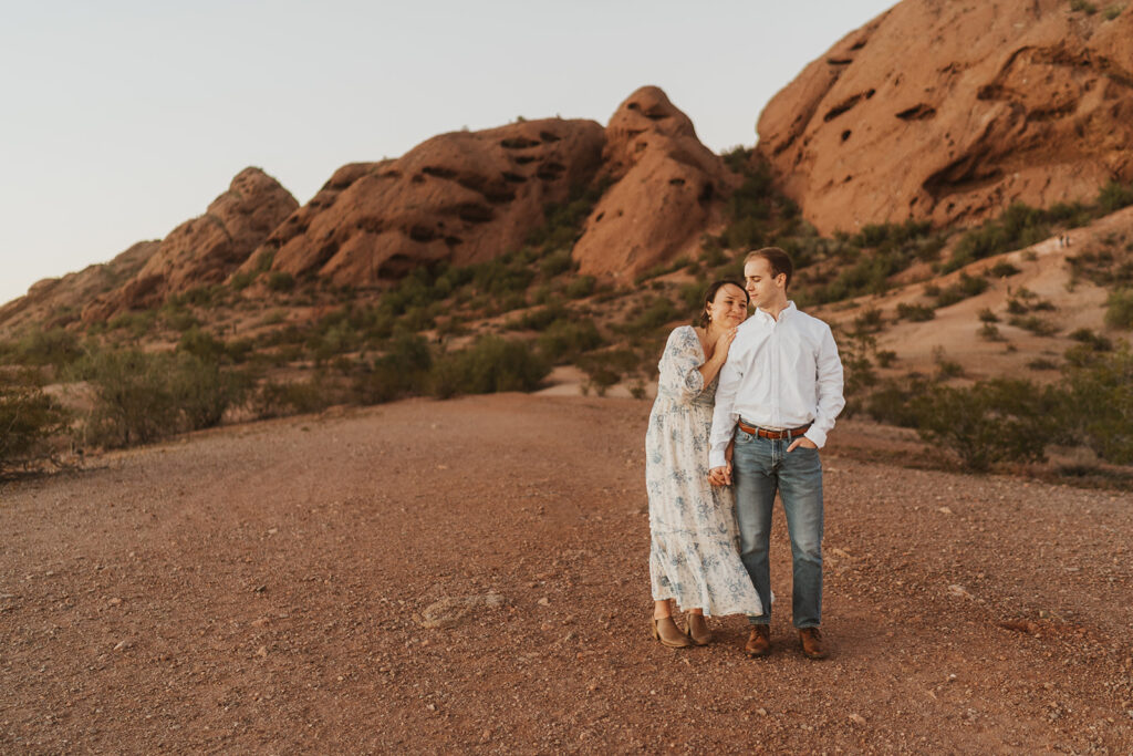 A man and a woman walk together in front of the red rocks of Papago Park