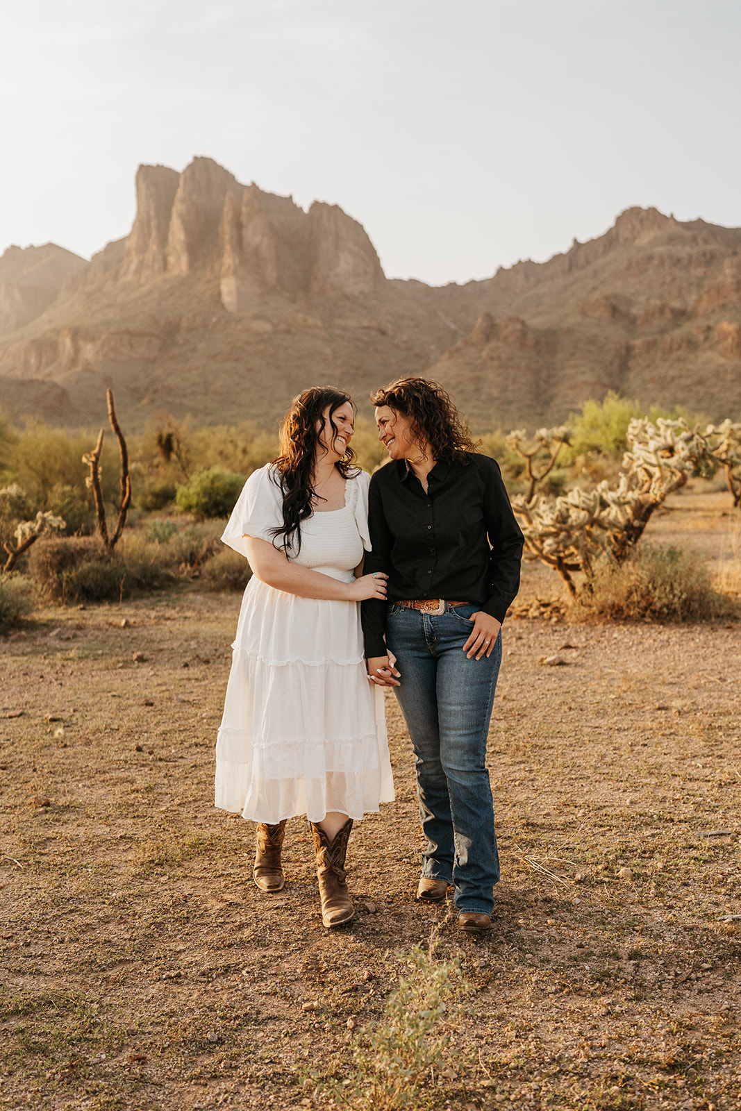 Two women walking in the desert holding hands and smiling at one another
